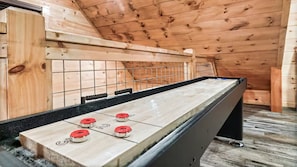 A shuffleboard table with four red discs, set in a wooden room with a sloped ceiling. - Scenic Log Retreat • HotTub, Indoor Pool & Dogs OK (Sevierville)