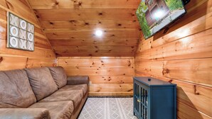 L'interno di una baita in legno, con un divano in pelle marrone, un piccolo armadietto e una televisione a parete.