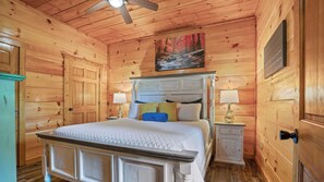 Un dormitorio de cabaña de madera con una cama con dosel, dos mesitas de noche y un ventilador de techo.