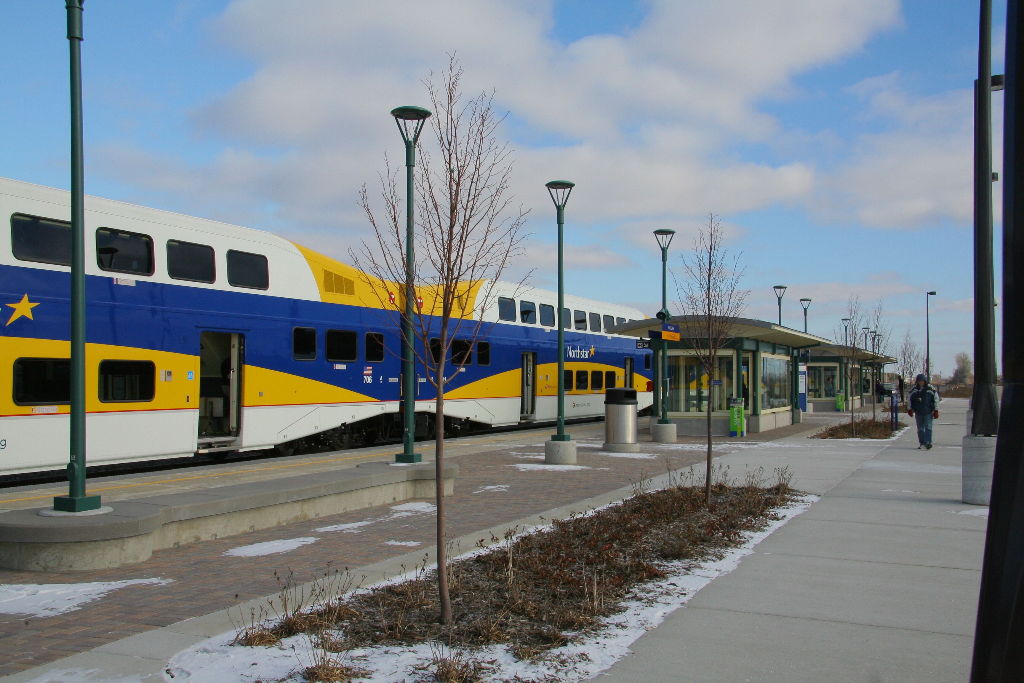 A train station platform with a stationary train, overhead shelter, and a pedestrian walkway.