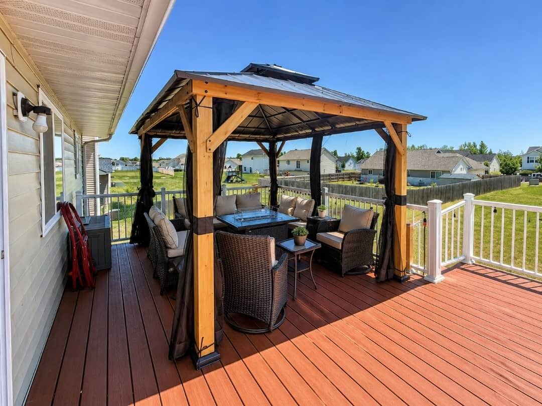 A covered outdoor deck with a table and chairs, a pergola, and a view of a residential neighborhood.