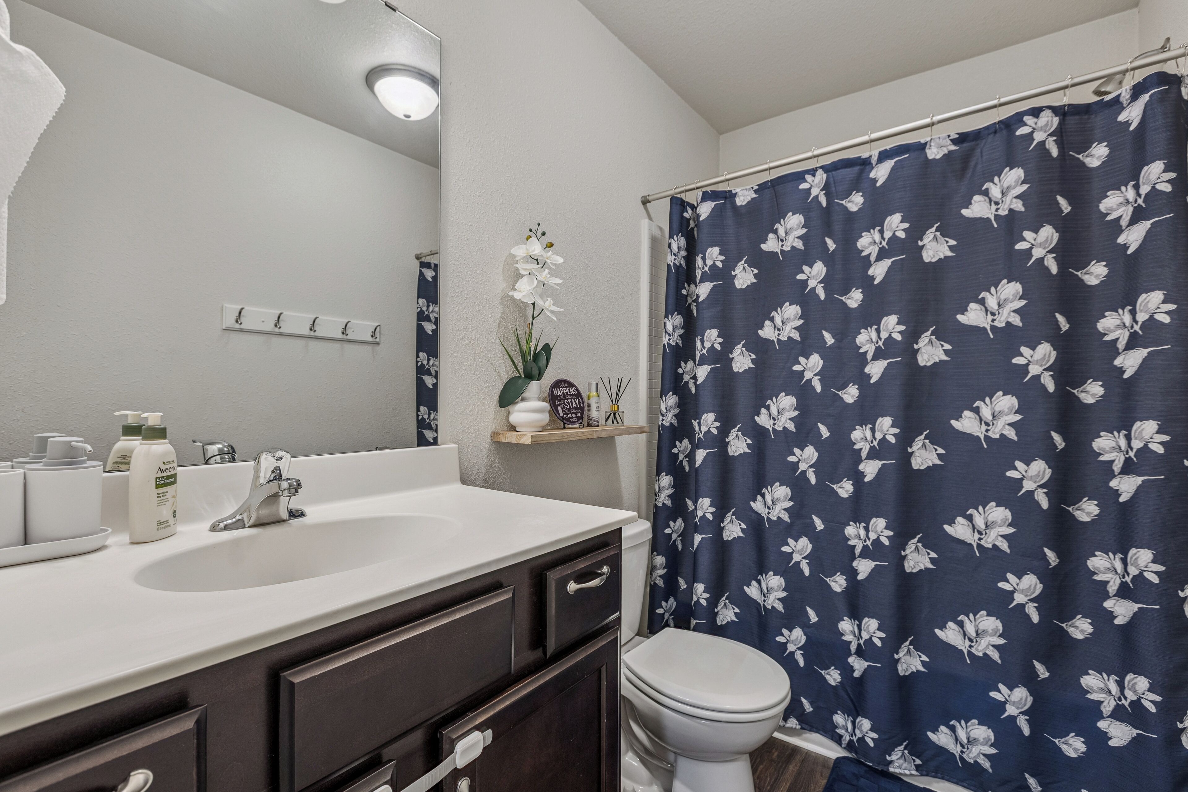 A bathroom with a white sink, dark cabinets, a toilet, and a shower curtain with a floral pattern.