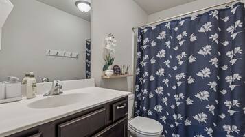 A bathroom with a white sink, dark cabinets, a toilet, and a shower curtain with a floral pattern.