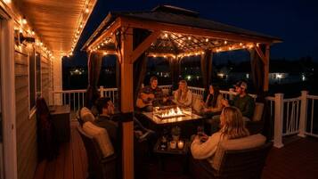 A covered outdoor seating area with a fire table, chairs, and string lights.