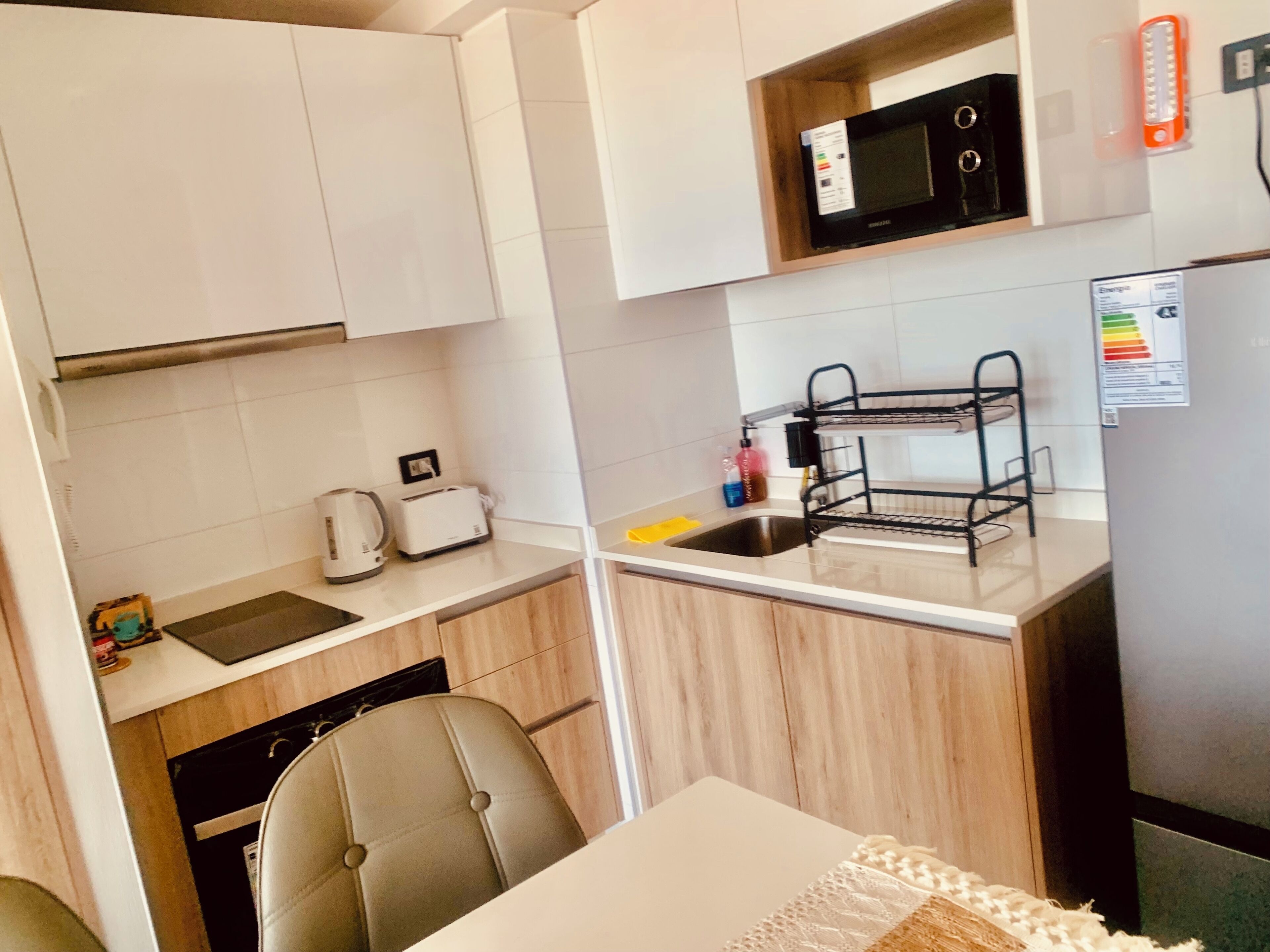 A compact kitchen with white cabinets, a microwave, a sink, a toaster, and a black metal rack.