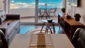 A modern living room with a large sliding glass door leading to a balcony overlooking the ocean. - Espectacular and Luminous Apartment face to face sea view in Iquique (Iquique)