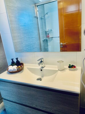 A bathroom with a white sink, a mirror, a glass shower enclosure, and a wooden door. - Espectacular and Luminous Apartment face to face sea view in Iquique (Iquique)