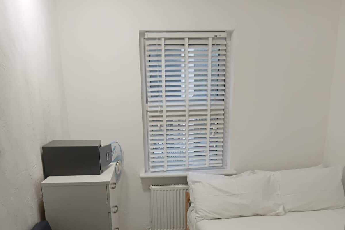 A small, compact room with a bed, a desk with a computer, a chair, and a radiator.