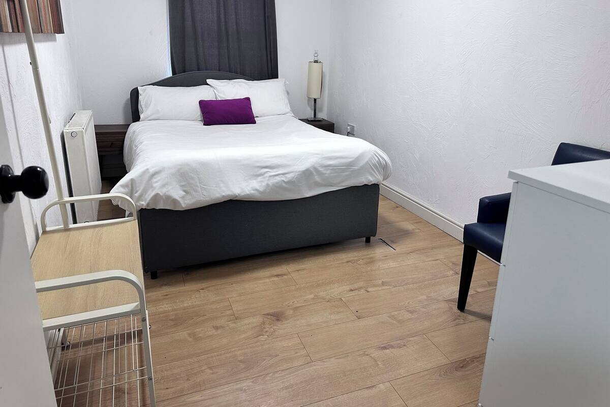 A bedroom with a bed, a bedside table with a lamp, a chair, and a radiator.