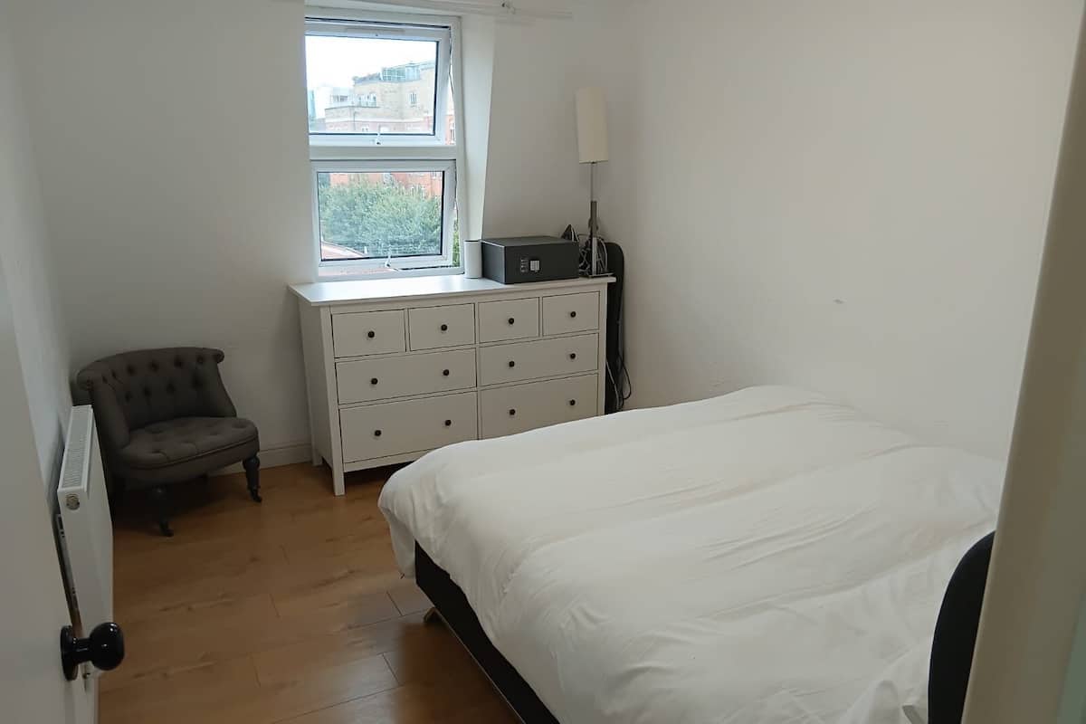 A bedroom with a bed, a dresser, a chair, and a radiator.