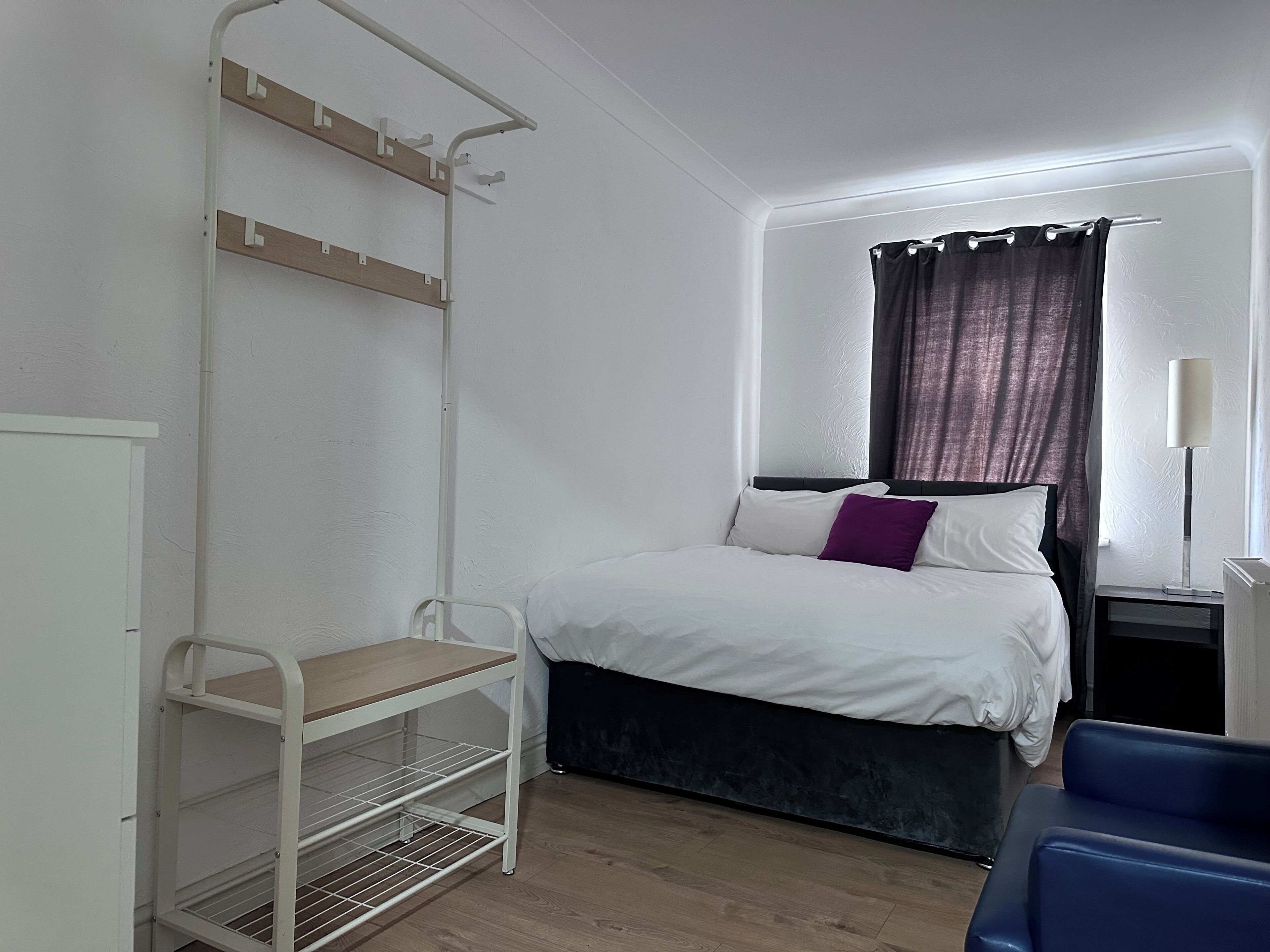 A bedroom with a bed, a nightstand, a lamp, a chair, and a white shelf unit.
