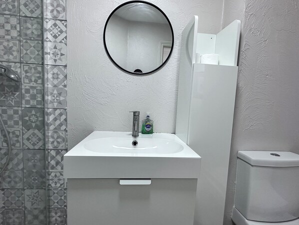 A bathroom with a white sink, a round mirror, and a toilet. - City Apartment Aldgate (London)