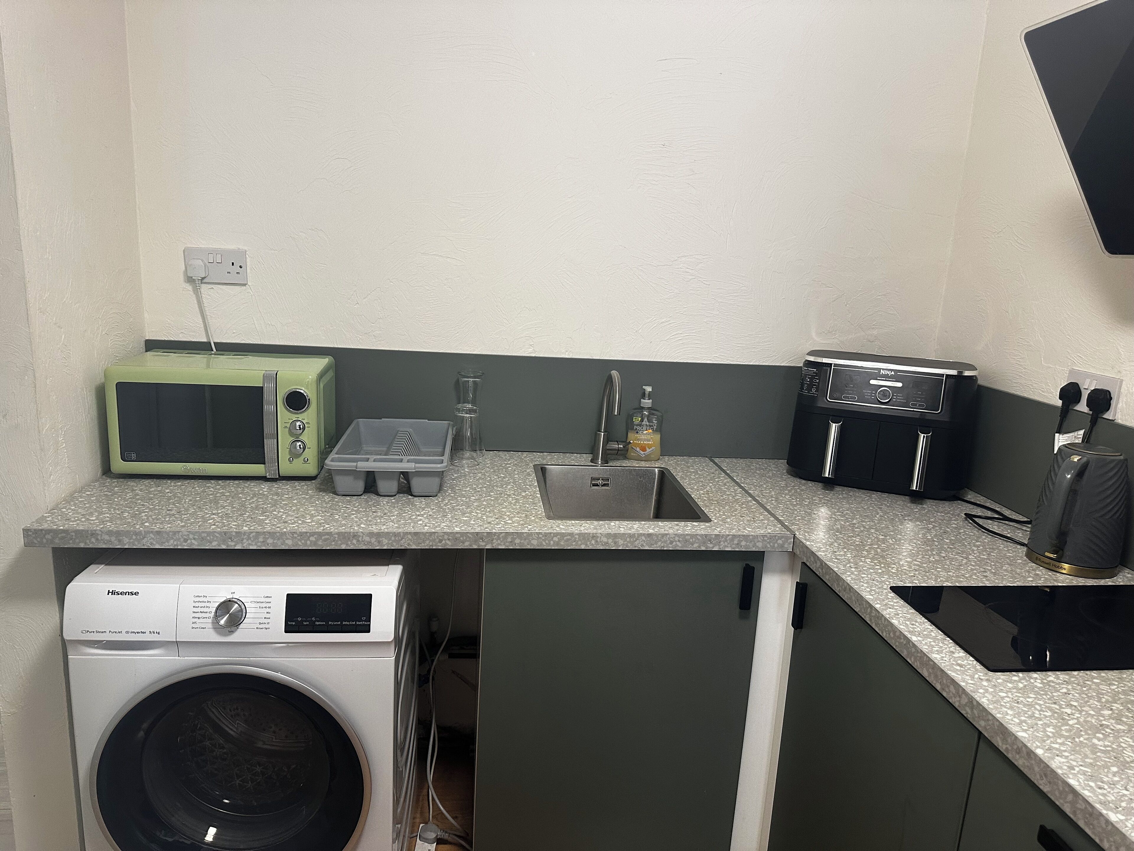 A compact kitchenette with a microwave, toaster, sink, and a washing machine.