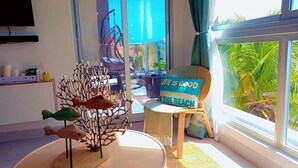 Una habitación con un gran ventanal, una silla con un cojín con motivos playeros y una escultura decorativa de un pez sobre una mesa.