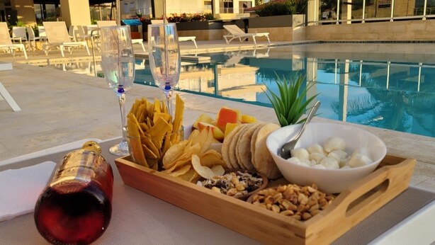 Escena junto a la piscina con una bandeja de aperitivos, un cuenco de nueces y dos copas de vino.