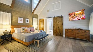 Een slaapkamer met een groot bed, houten wanden, een televisie, een dressoir en een schuifdeur in boerderijstijl.