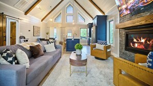 Een ruime woonkamer met een hoge plafond, een open haard, en een keuken die zichtbaar is door een open deur.