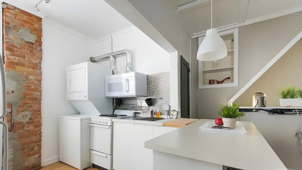 A modern kitchen with white cabinetry, a brick wall, and a small island with seating. - Penthouse @ Palmer Park W/D, AC, Fast WiFi, PrivateRoofDeck in Fabulous Fishtown (Philadelphia)