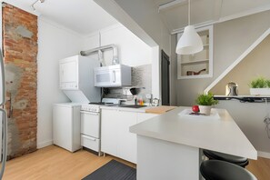 A modern kitchen with white cabinetry, a brick wall, and a small island with seating. - Penthouse @ Palmer Park W/D, AC, Fast WiFi, PrivateRoofDeck in Fabulous Fishtown (Philadelphia)