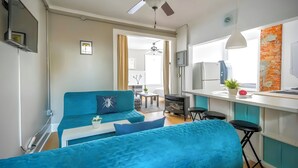 A modern living room with a blue sofa, a ceiling fan, and a kitchen area with a white countertop and bar stools. - Penthouse @ Palmer Park W/D, AC, Fast WiFi, PrivateRoofDeck in Fabulous Fishtown (Philadelphia)