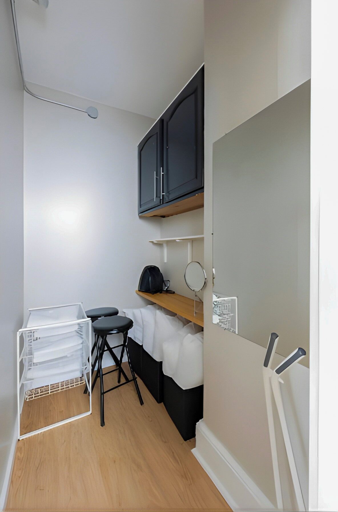 A small, compact room with a kitchenette, a black cabinet, a mirror, and a stool.