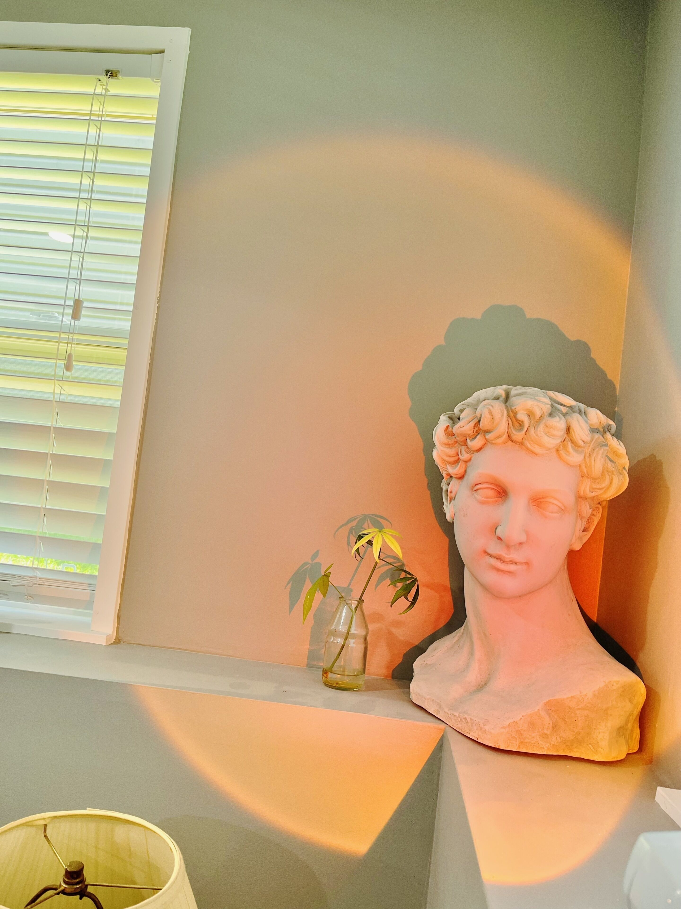 Une pièce avec une fenêtre, une lampe, une sculpture et un vase contenant une plante.