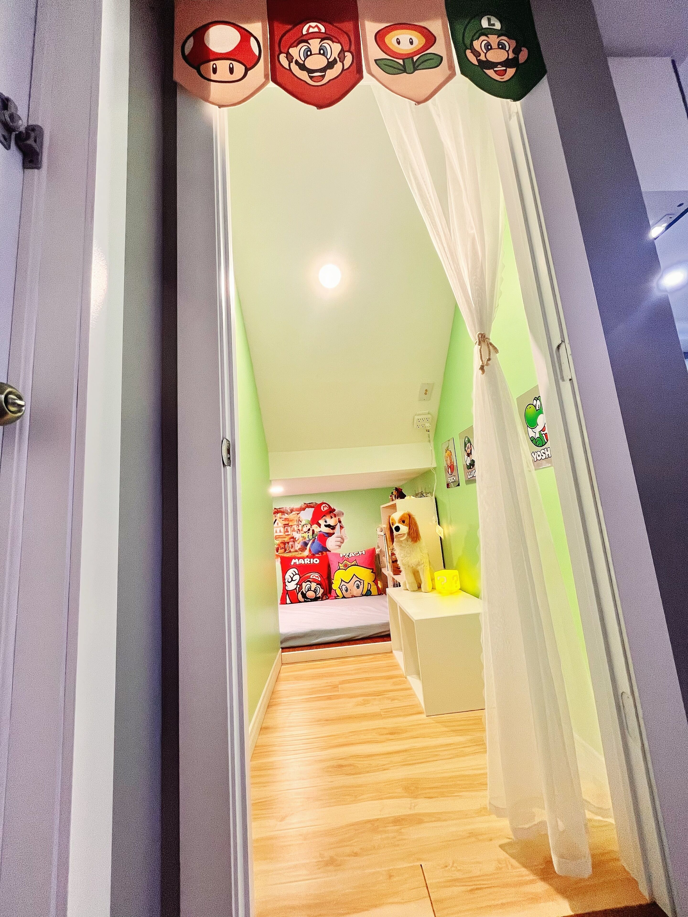 Ein schmaler Flur mit einem Bett, das mit Mario- und Luigi-Postern, einem kleinen Hund und einem weißen Schrank dekoriert ist.