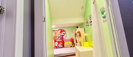 Ein schmaler Flur mit einem Bett, das mit Mario- und Luigi-Postern, einem kleinen Hund und einem weißen Schrank dekoriert ist.