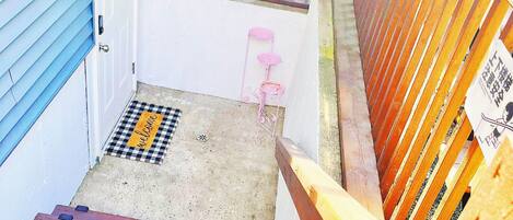 Un escalier en bois menant à une véranda couverte, agrémentée d’une rambarde en métal.