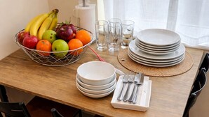 Una mesa de comedor dispuesta con platos, vasos, cubiertos y una cesta de frutas.