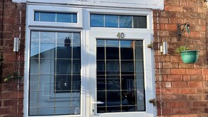 A white door with the number 40, a window with a grid pattern, and a green hanging planter on a brick wall. - 4 Bed House-Sleeps 7-Free Parking (Birmingham)
