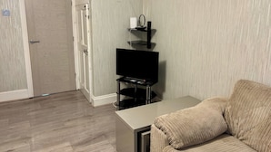 A living room with a television on a stand, a sofa, and a door. - 4 Bed House-Sleeps 7-Free Parking (Birmingham)