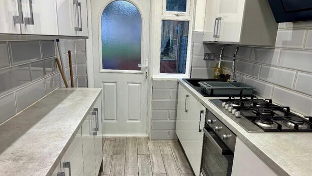 A kitchen with white cabinets, a stove, and a window with a view. - 4 Bed House-Sleeps 7-Free Parking (Birmingham)