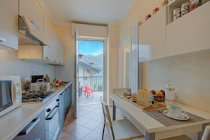 Una cocina estrecha con vistas al exterior, un comedor con una mesa dispuesta para dos personas y un pequeño balcón con una silla.