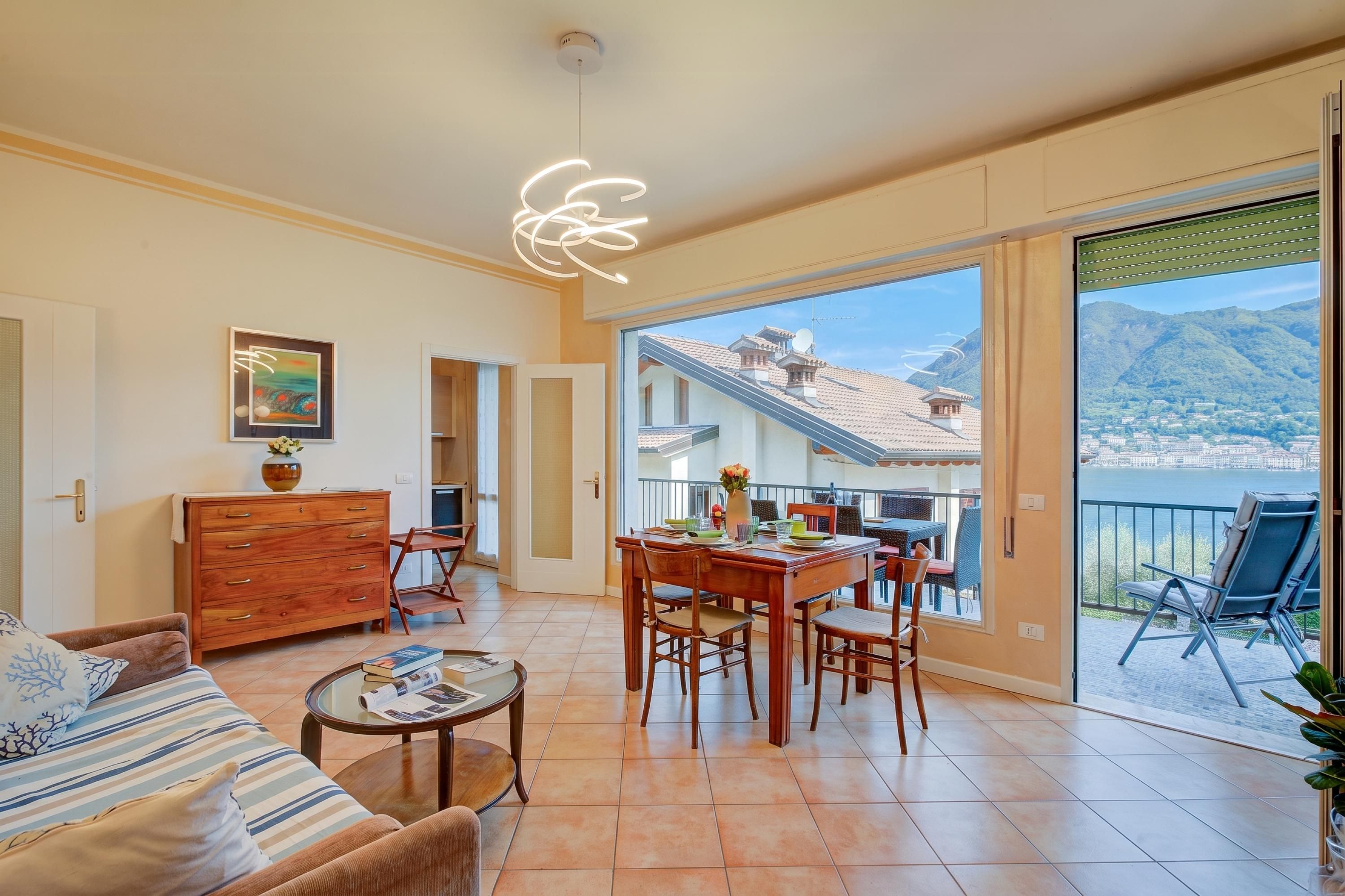 A spacious living area with a dining table, sofa, and a view of a mountainous landscape through large windows.