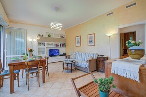 Una sala de estar con televisor, sofá, mesa de comedor, sillas y una planta en maceta.