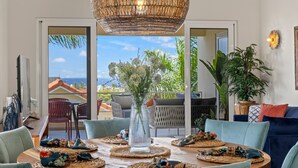 A dining area with a round table, wicker placemats, and a clear vase with flowers. - Palm Piscadera · Ocean Views · Pool · Beaches (Piscadera)