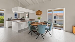 A modern kitchen with a central island, light blue chairs, and a hanging rattan light fixture. - Palm Piscadera · Ocean Views · Pool · Beaches (Piscadera)