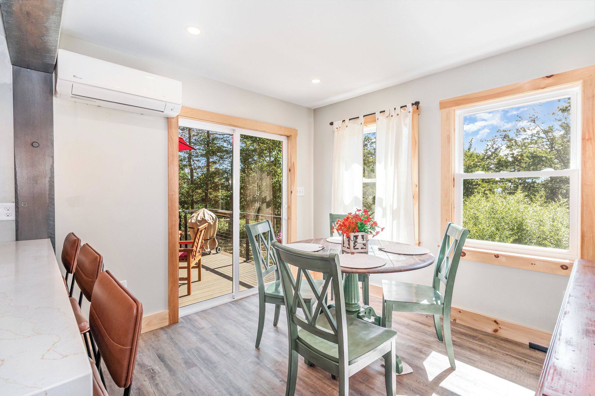 A dining area with a table and chairs, a view of the outdoors through a glass door, and an air conditioning unit on the wall.