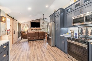 A modern kitchen with dark cabinets, stainless steel appliances, and a fireplace. - Whispering Pines Cabin Cozy Forest Cabin Retreat (Biglerville)