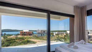 A modern hotel room with a large balcony, a bed with neatly made towels, and a view of the sea and buildings. - Palm Villa Petra with Pool, Medulin, Croatia (Medulin)