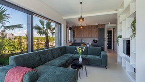 A modern living room with a sectional sofa, a small round table, and a view of the kitchen and outdoor area. - Palm Villa Petra with Pool, Medulin, Croatia (Medulin)