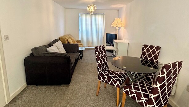 A compact living space with a sofa, a dining table with chairs, a TV, and a lamp. - 2 Bed Wolverhampton Apartment-sleeps 5 (Wolverhampton)