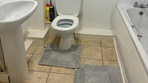 A bathroom with a toilet, sink, and bathtub. There are two gray rugs on the floor. - 2 Bed Wolverhampton Apartment-sleeps 5 (Wolverhampton)