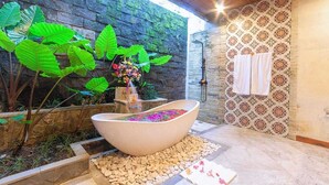A spa area with a large freestanding bathtub filled with flowers, surrounded by a stone wall and lush greenery. - Nidhi serene villa ubud (Kabupaten Gianyar)