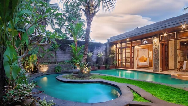 A pool surrounded by tropical plants, a stone wall, and a building with large windows and a bed visible inside. - Nidhi serene villa ubud (Kabupaten Gianyar)