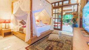 A four-poster bed with a canopy, a wooden nightstand with a lamp, a large window with a view of greenery, and a flat-screen TV on a wooden table. - Nidhi serene villa ubud (Kabupaten Gianyar)