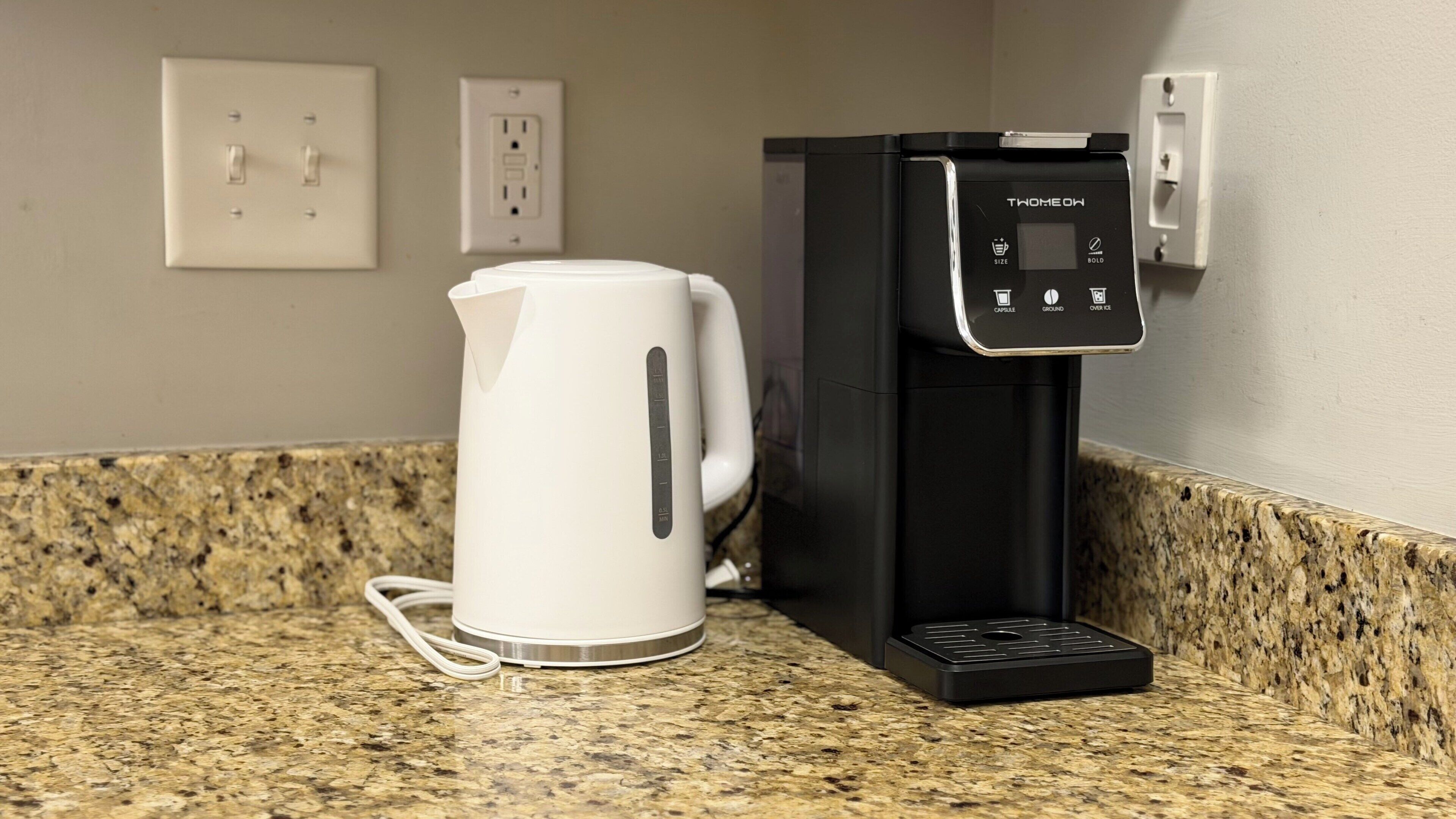 A coffee machine and a white electric kettle on a granite countertop.
