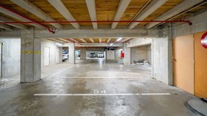 A parking garage with concrete pillars, a wooden ceiling, and a red pipe running across the ceiling. - Large Stylish 1BR Apartment + Carpark in CBD (Auckland Central)