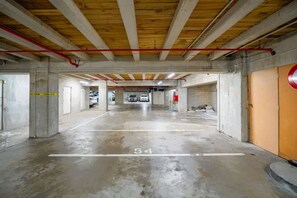 A parking garage with concrete pillars, a wooden ceiling, and a red pipe running across the ceiling. - Large Stylish 1BR Apartment + Carpark in CBD (Auckland Central)